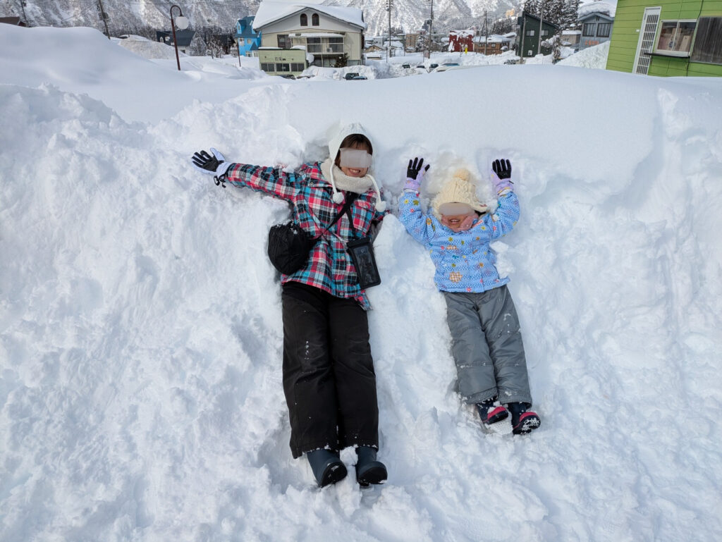 深雪の中に身体を埋めて仰向けに寝転び、手を広げて楽しむ親子の様子