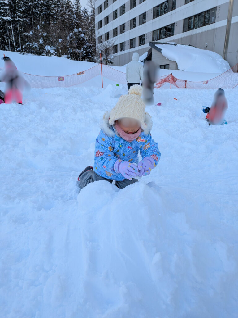 エンゼルグランディア越後中里のホテル前ゲレンデで、夢中で雪玉をつくる小さな女の子