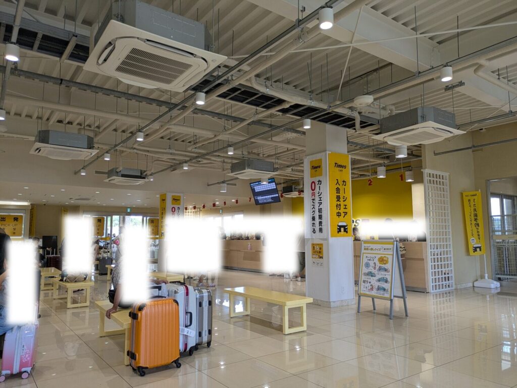 広々としたタイムズレンタカー那覇空港店の受付ロビーとスーツケースを置いて待つ利用者の様子