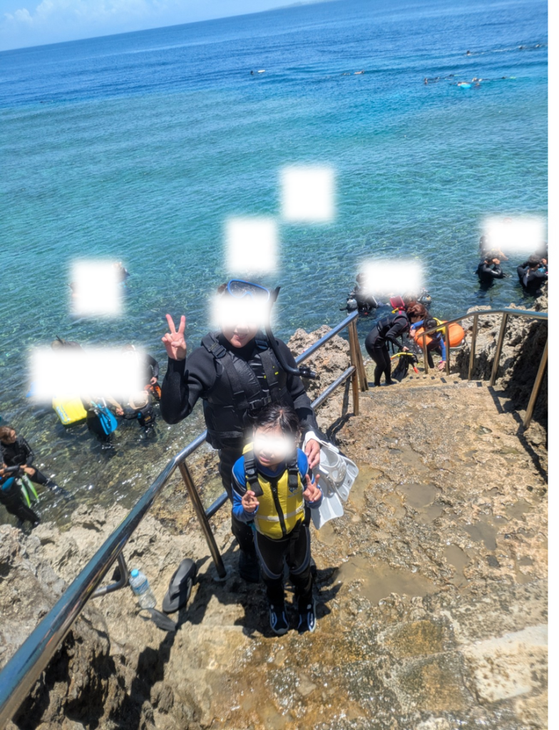 青の洞窟（真栄田岬）の海へと降りる岩場階段で、ウェットスーツを着用し海に入る直前にピースサインをする親子。