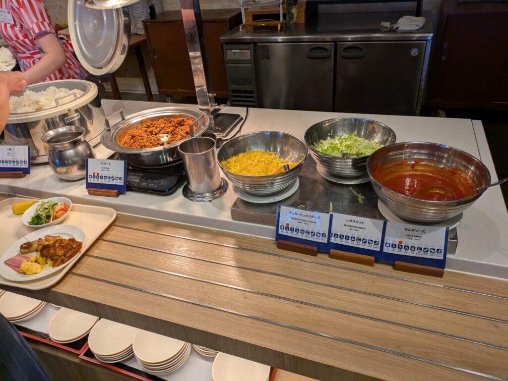 タコミートやチーズ、レタス、サルサソースが並ぶビュッフェのタコライス作りコーナー