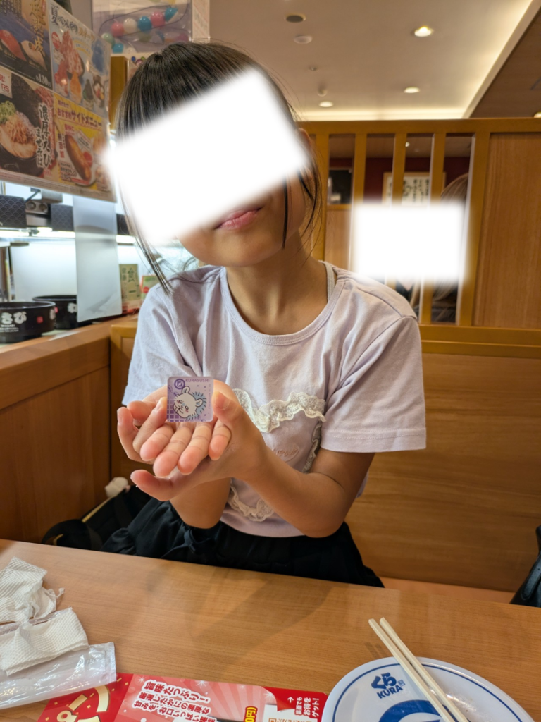 くら寿司の店内で、ビッくらポンで当たったちいかわモモンガのマグネットを両手で大切そうに持つ子ども
