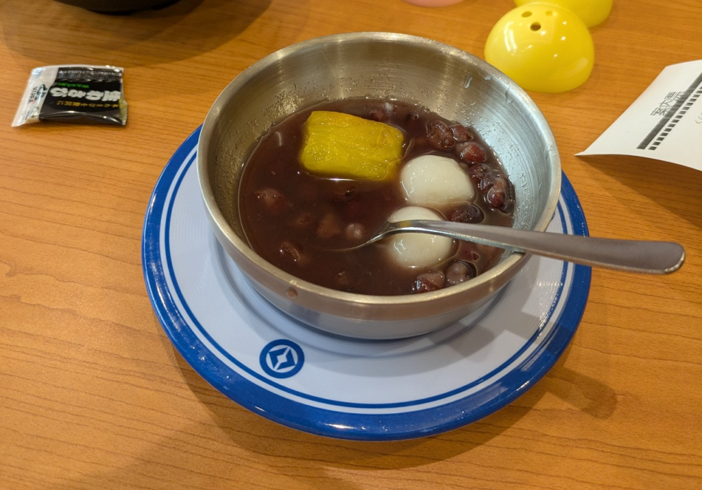 くら寿司の寿司皿に乗って運ばれてきた冷やしぜんざいと、テーブルに置かれたビッくらポンのカプセル