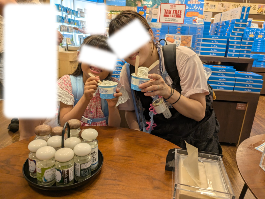 那覇空港の塩屋(まーすやー)でトッピング塩のボトルが並ぶテーブルを囲み雪塩ソフトクリームを持つ親子