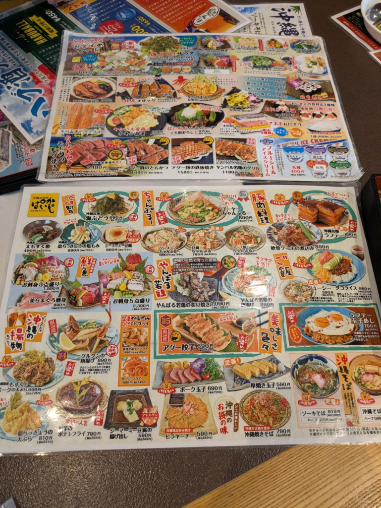 沖縄居酒屋「沖縄の台所 ぱいかじ」のフードメニュー表。ちゃんぷるーやラフテー、アグー餃子などの沖縄名物料理が写真付きで並んでいる。