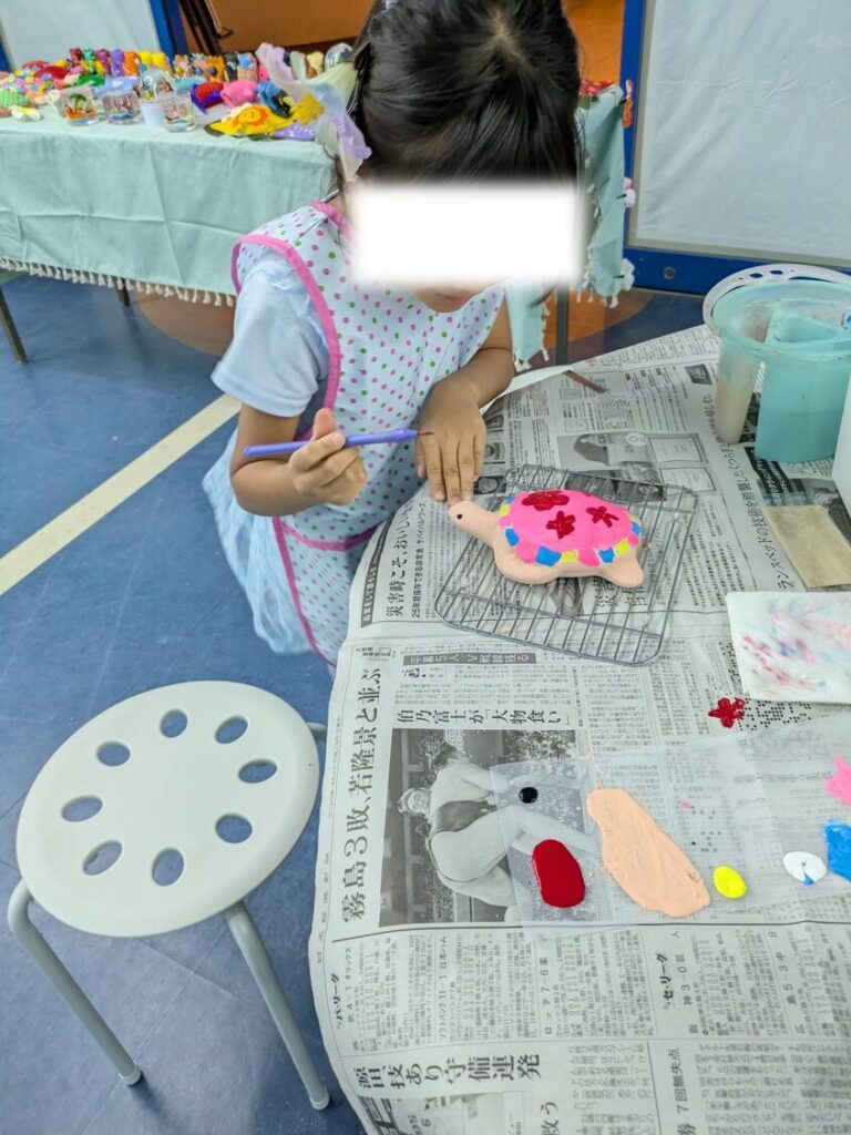 リザンシーパークホテルの絵付け体験で、筆を使ってピンクや黄色でカメの置物に色を塗る娘。