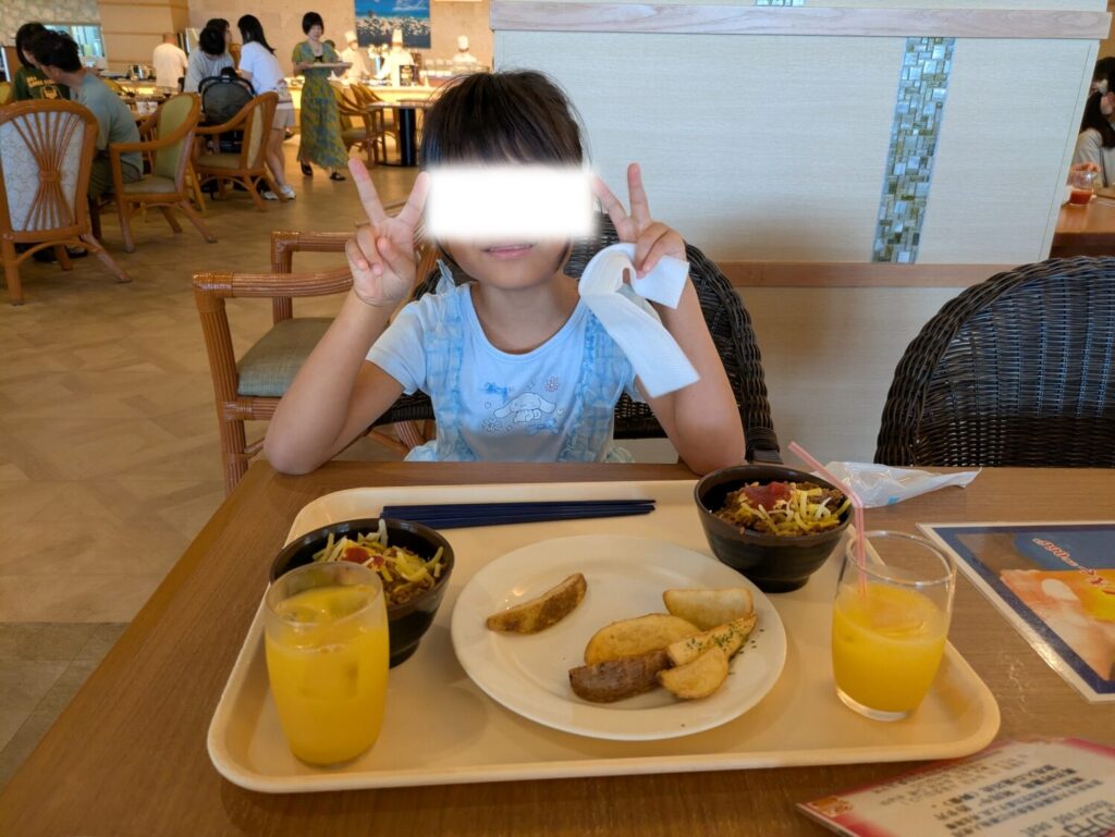 リザンシーパークホテル谷茶ベイのシーサイドレストラン「谷茶ベイ」で、朝食バイキングの料理を前に両手でピースサインをする娘。
