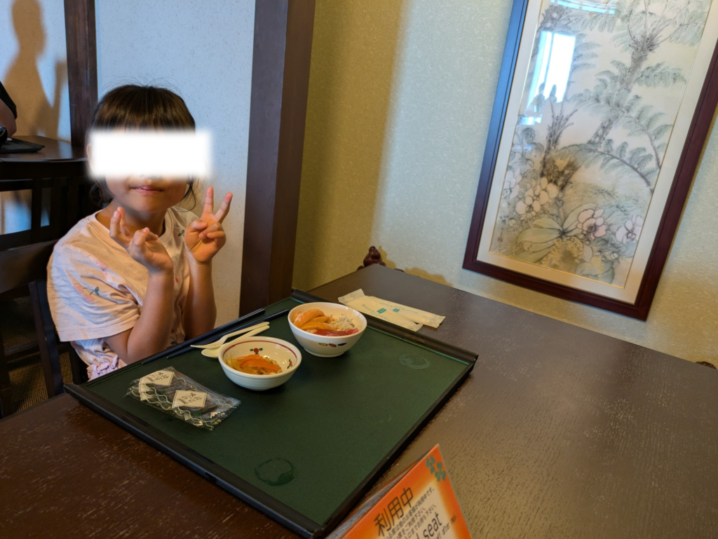 朝食会場「七福」のテーブル席で海の幸を前に笑顔でピースサインをする子ども