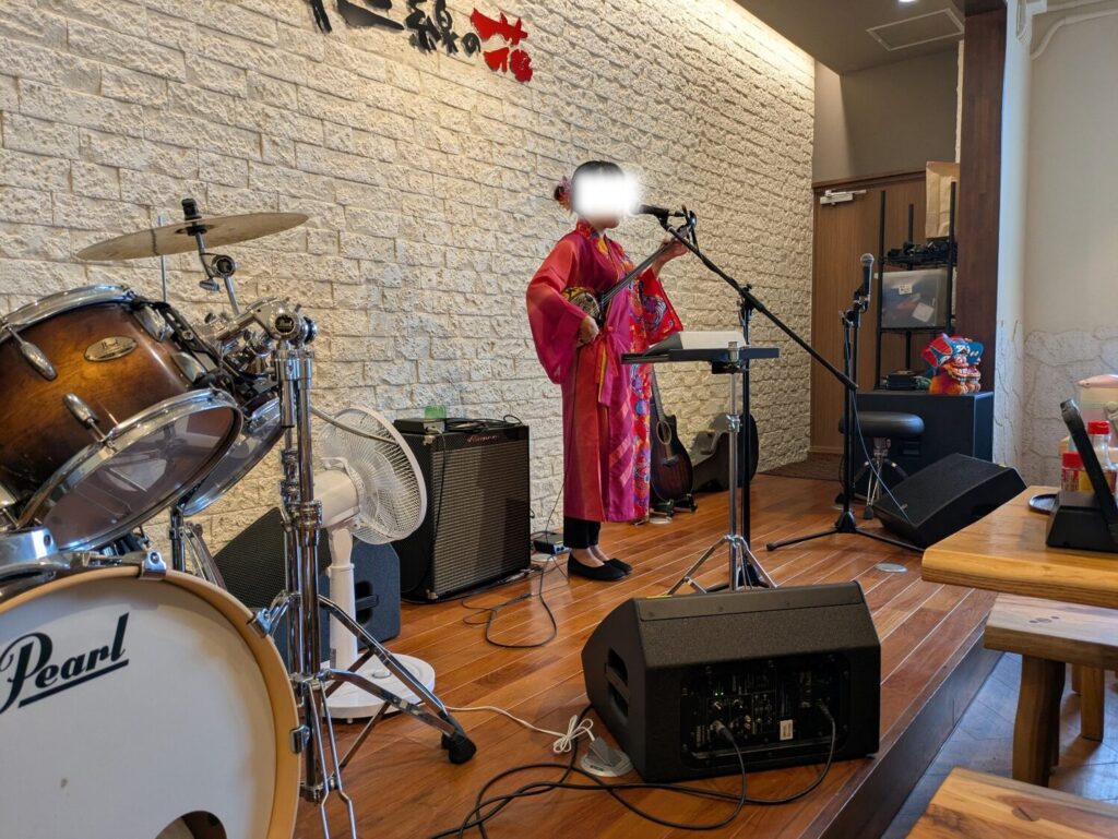 沖縄居酒屋のステージで三線を演奏する琉装姿の女性アーティスト