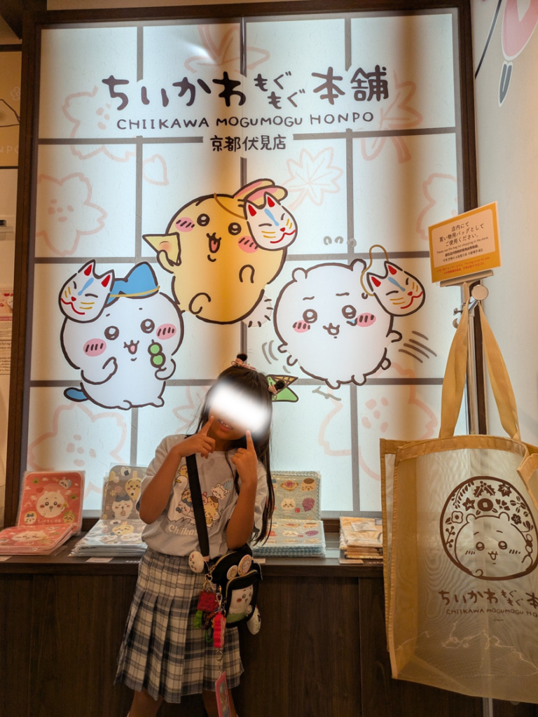 ちいかわもぐもぐ本舗 京都伏見店の店内で障子風のパネルを背景にポーズをとる娘