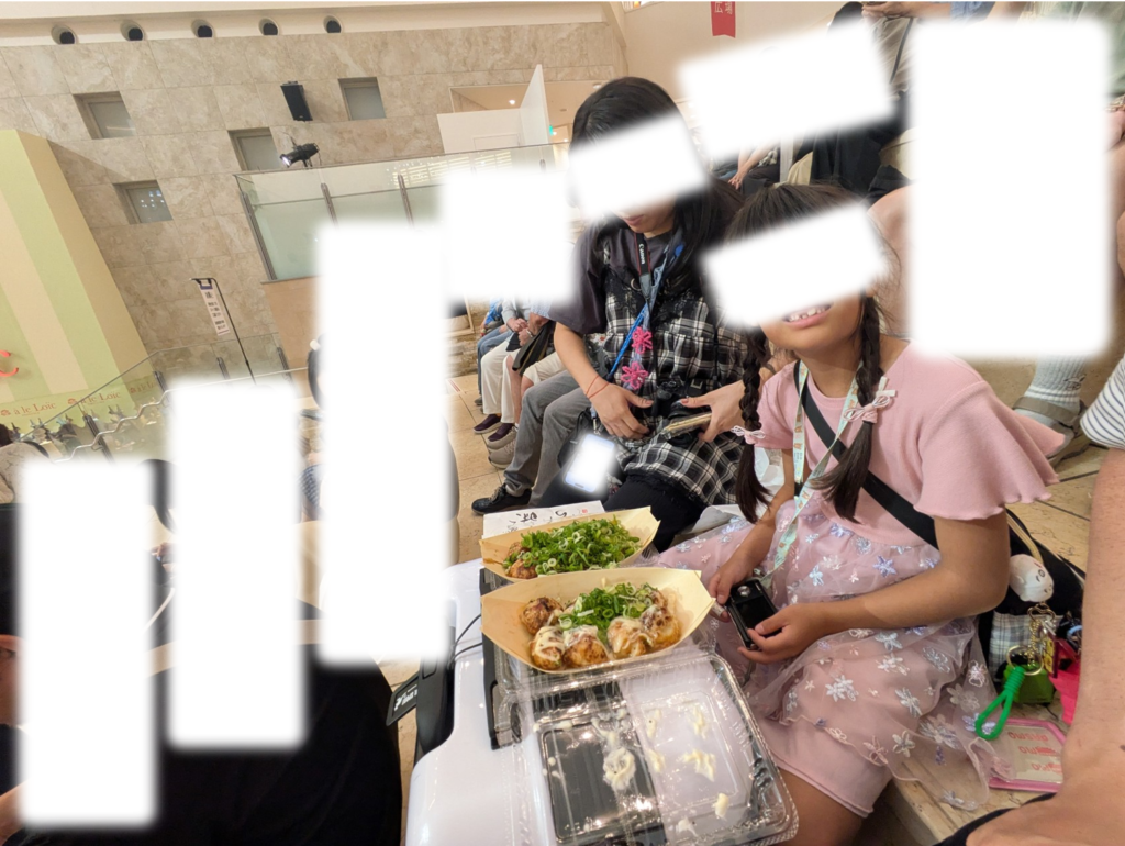 阪急うめだ本店9階の大階段スペースで「はなだこ」で購入したテイクアウトのたこ焼きを食べる家族の様子