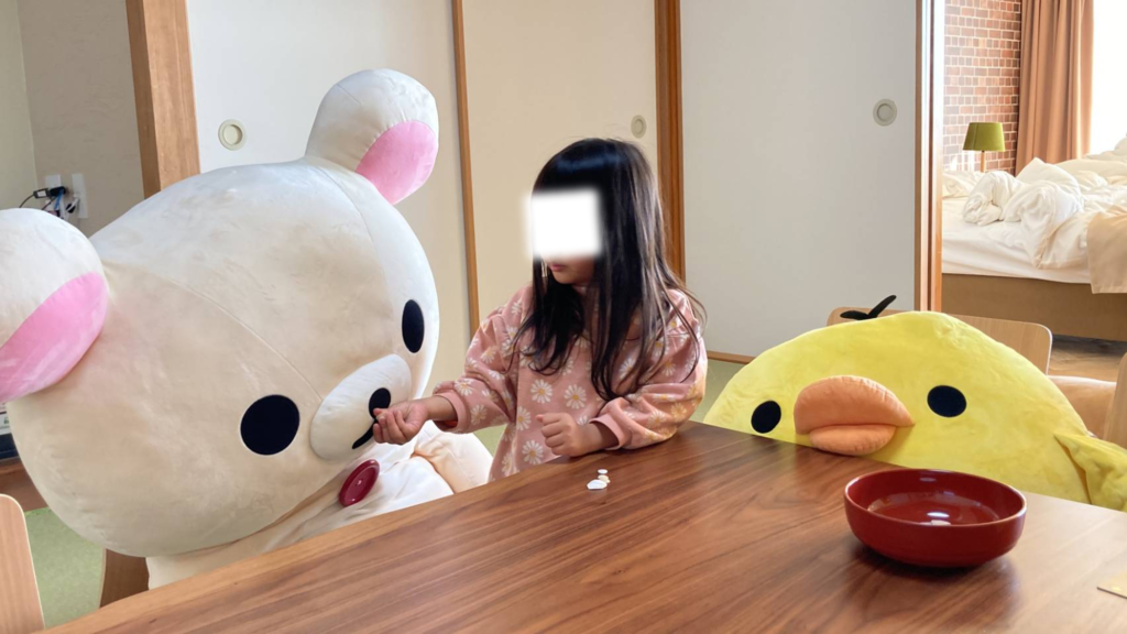 マホロバ・マインズ三浦のリラックマルーム和室にて、大きなコリラックマやキイロイトリのぬいぐるみに囲まれて座卓で遊ぶ子どもの姿