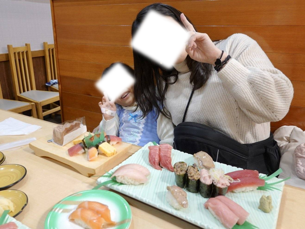 テーブルいっぱいに並んだ新鮮なお寿司を前に、ランチタイムに笑顔でピースサインをする親子の姿