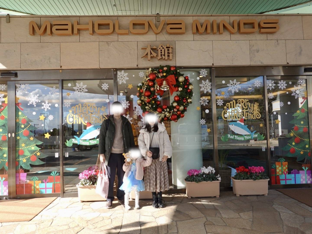マホロバ・マインズ三浦の本館エントランス前。大きなクリスマスリースや装飾が施された自動ドアの前で記念撮影をする家族の姿