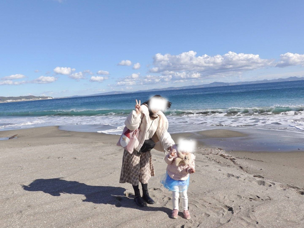 青空と海が広がる三浦海岸の砂浜で、手を繋いでピースサインをする親子の姿
