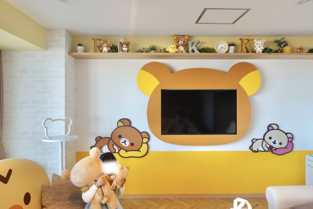 マホロバ・マインズ三浦のリラックマルーム。リラックマ型の枠が付いた壁掛けテレビの前で、大きなぬいぐるみを抱きかかえる子どもの姿