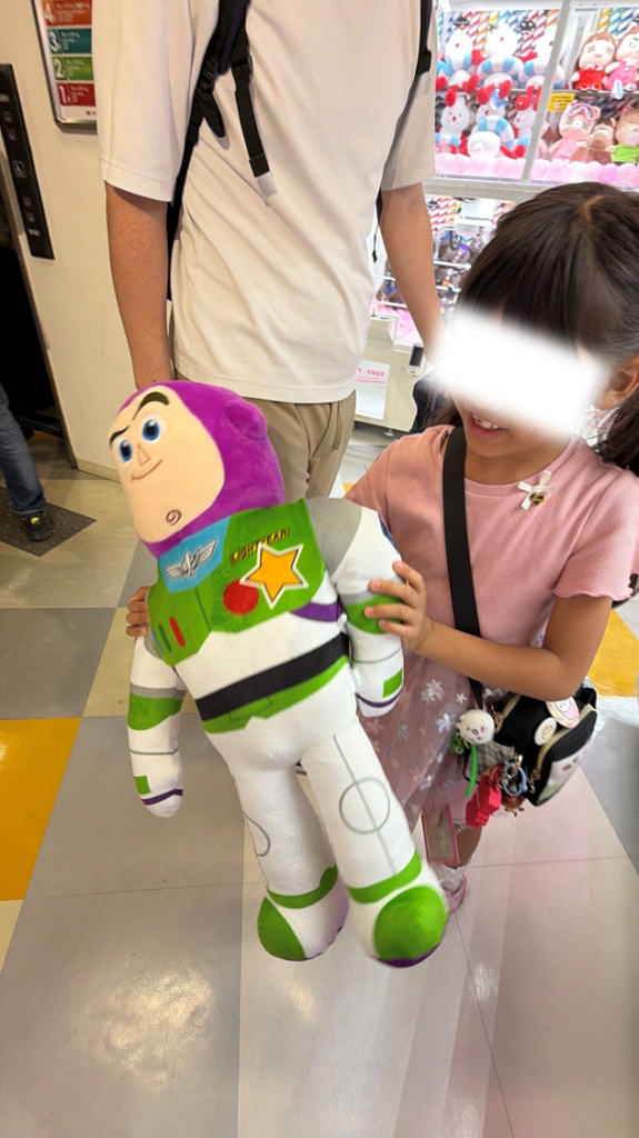 タイトーステーションなんば店でゲットした特大バズ・ライトイヤーのぬいぐるみと喜ぶ女の子